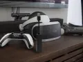 Czarny adapter PlayStation Camera z niebieską diodą, obok gogli VR i kontrolera.
