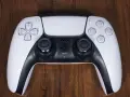 Biały kontroler DualSense do PS5 leży na drewnianym blacie. Zastanawiasz się nad ps4 pobór prądu?