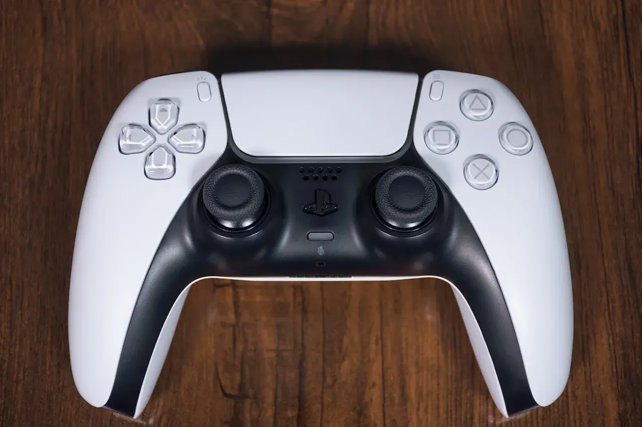 Biały kontroler DualSense do PS5 leży na drewnianym blacie. Zastanawiasz się nad ps4 pobór prądu?