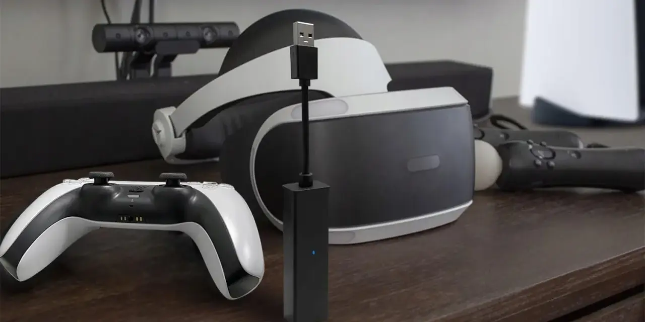 Czarny adapter PlayStation Camera z niebieską diodą, obok gogli VR i kontrolera.
