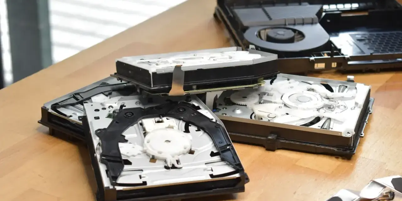 Rozłożone wnętrze konsoli PS4 Slim, widać dysk i mechanizm napędu. Komponenty leżą na drewnianym blacie, przypominając o kompaktowych ps4 slim wymiary.