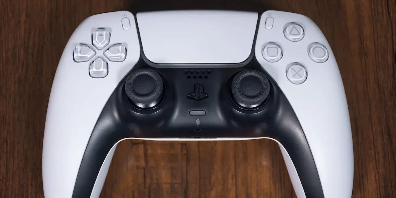 Biały kontroler DualSense do PS5 leży na drewnianym blacie. Zastanawiasz się nad ps4 pobór prądu?