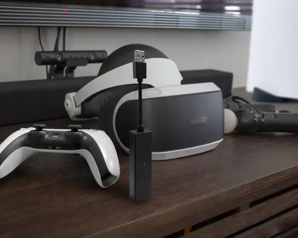 Czarny adapter PlayStation Camera z niebieską diodą, obok gogli VR i kontrolera.