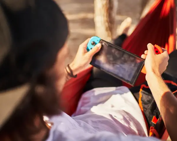 Osoba w hamaku gra na Nintendo Switch. Czas ładowania konsoli jest krótki, więc można grać wszędzie.