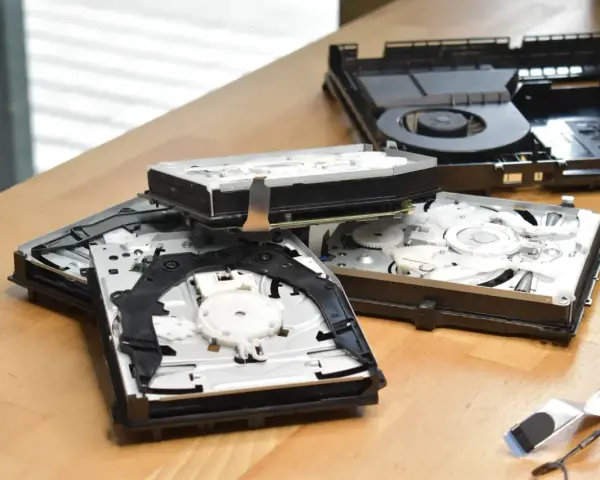 Rozłożone wnętrze konsoli PS4 Slim, widać dysk i mechanizm napędu. Komponenty leżą na drewnianym blacie, przypominając o kompaktowych ps4 slim wymiary.