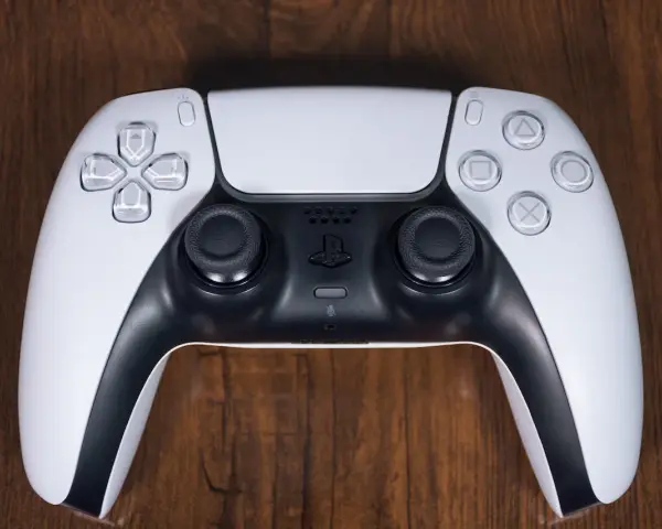 Biały kontroler DualSense do PS5 leży na drewnianym blacie. Zastanawiasz się nad ps4 pobór prądu?