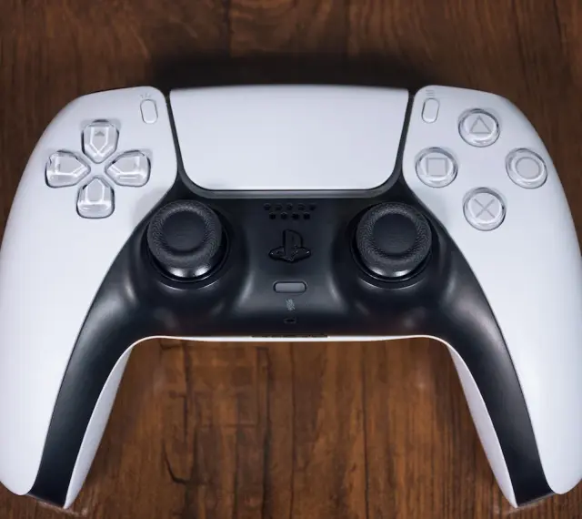 Biały kontroler DualSense do PS5 leży na drewnianym blacie. Zastanawiasz się nad ps4 pobór prądu?