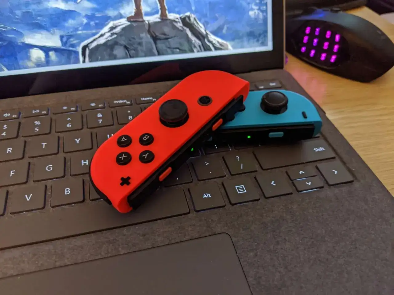 Czerwony i niebieski Joy-Con na klawiaturze laptopa, gotowe do gry. Dowiedz się, jak podłączyć pada od Nintendo Switch do PC.