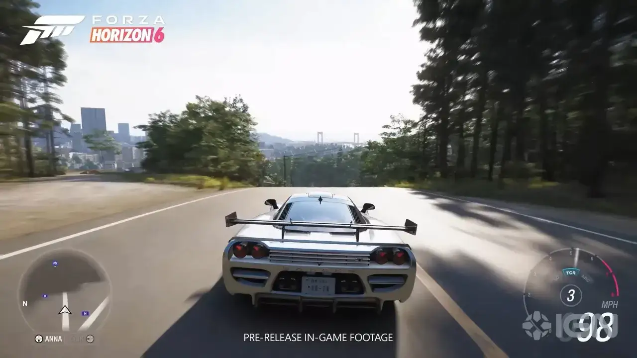 Biały supersamochód pędzi po krętej drodze w Forza Horizon 6 na PS5. W tle widać miasto i most.
