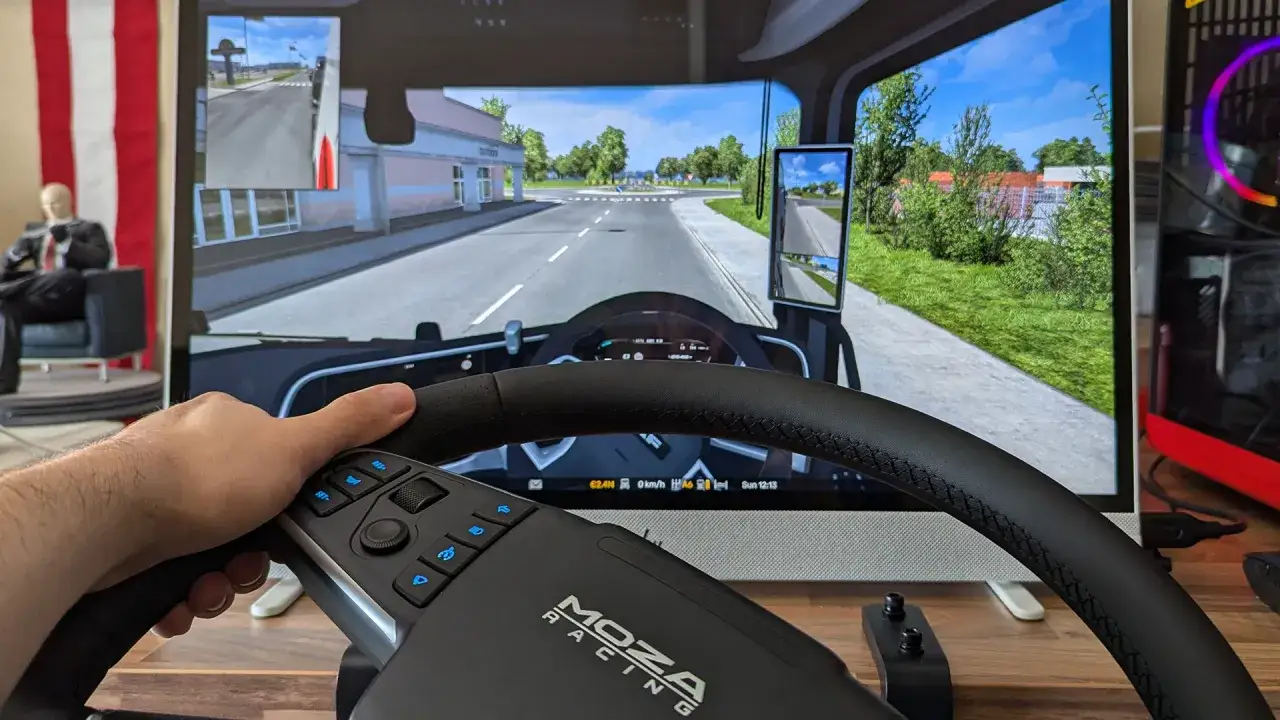 Ręka trzyma kierownicę MOZA Racing, grając w Euro Truck Simulator 2 na PS5. Wirtualna ciężarówka jedzie przez słoneczne miasteczko.